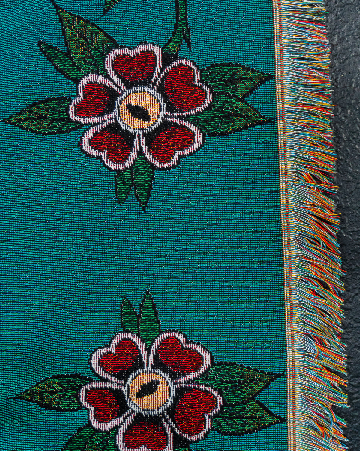 Textile with floral patterns and fringe on a teal background