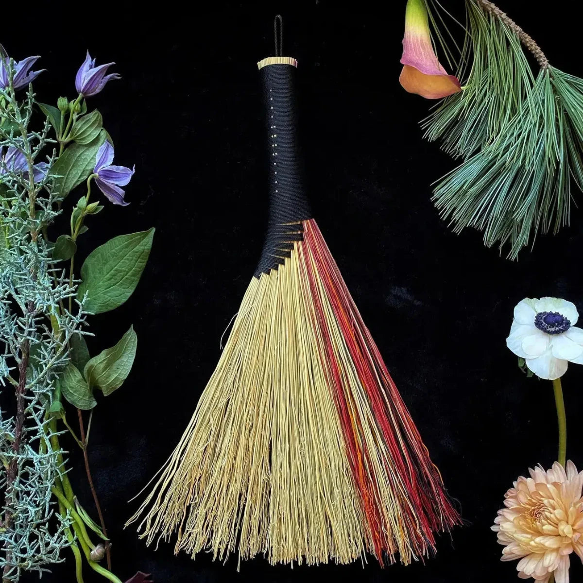 A woven handmade broom with natural colors and black cord.