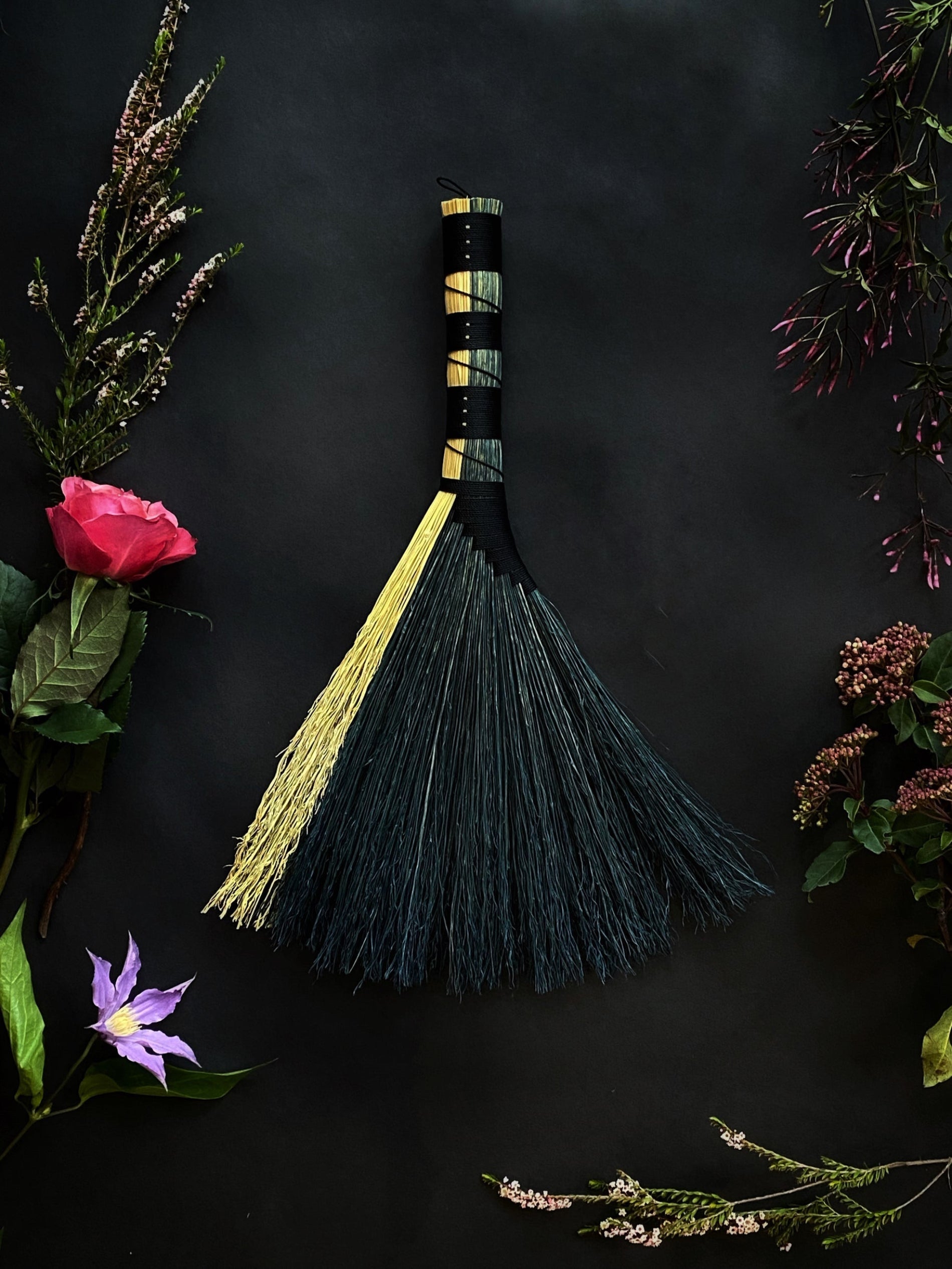 Decorative broom with a yellow handle and black bristles on a dark background with flowers.