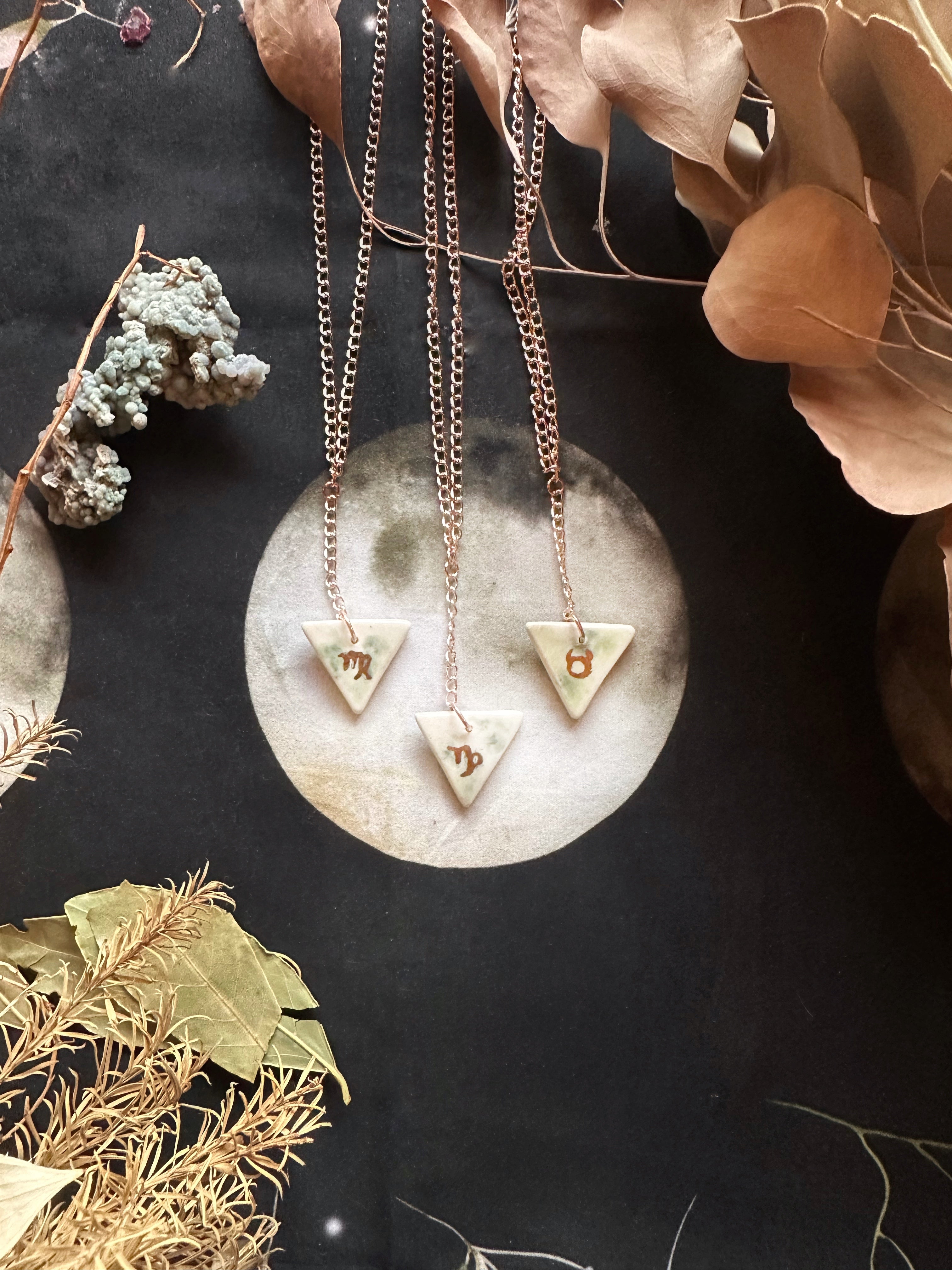 This handmade porcelain earth based zodiac pendant is 1” x 1”, double sided with an elemental symbol and the zodiac sign. It has a 20” chain champagne gold plated iron chain - Portland, OR by Keven Craft Rituals.