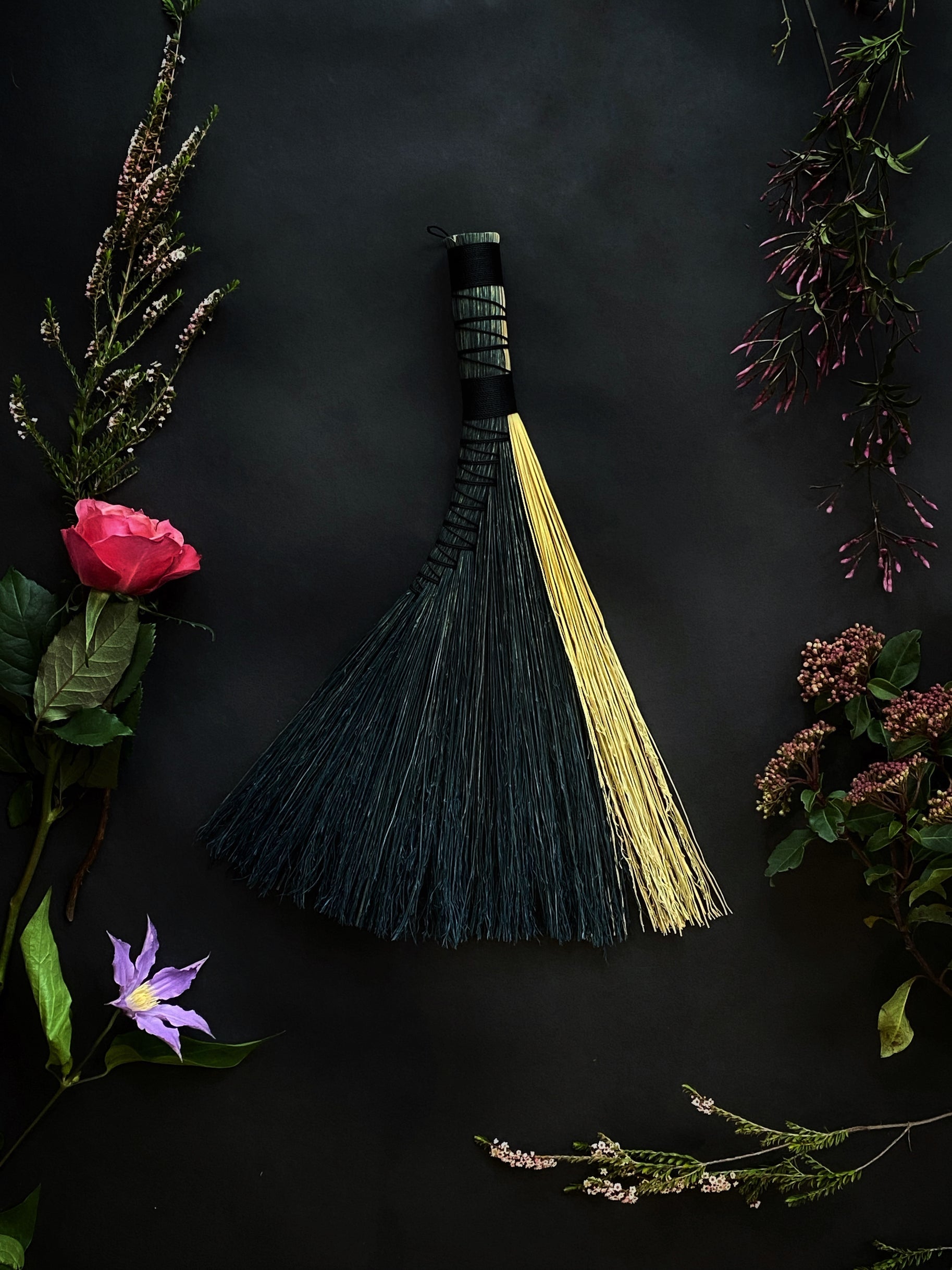 A black and natural woven hand broom shaped as a turkey style wing by Keven Craft Rituals.